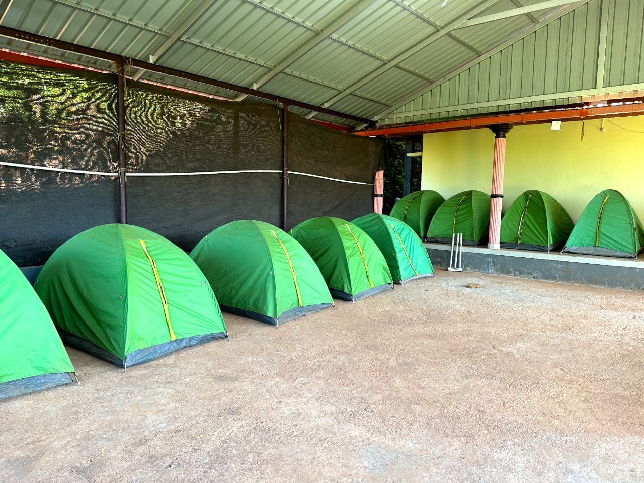 Row of green tent houses under a covered shed at Satish Mullodi Home Stay in Mullodi, Kudremukh